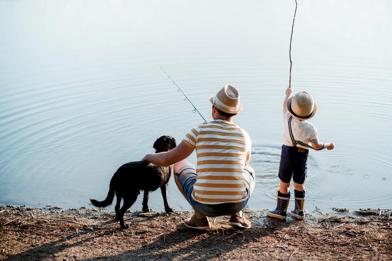 Far, søn og hunf der fisker ved vandkanten