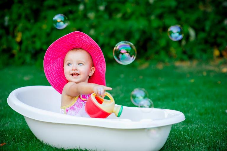 Babypige med stor hat sidder i badekar på græsplane
