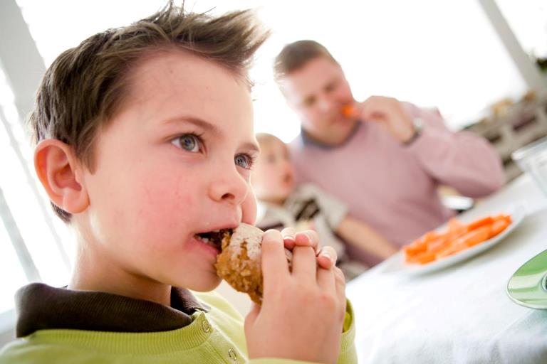 Dreng der putter mad i munden med far og bror bagved