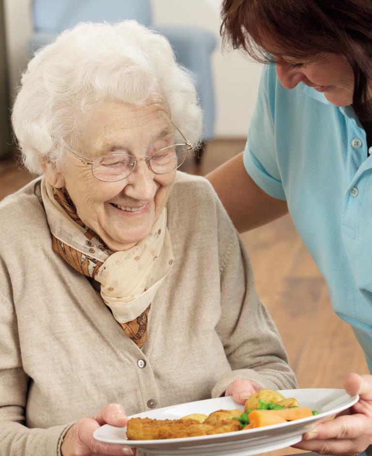 En ældre dame som får serveret en tallerken med mad.