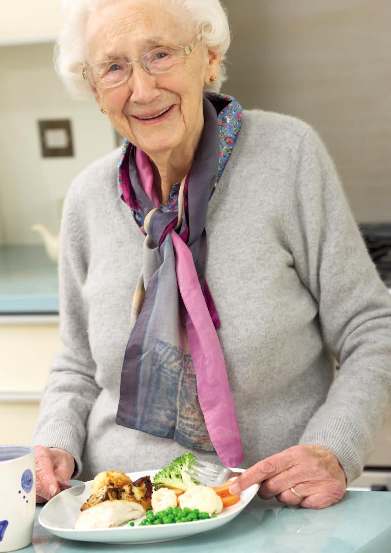 En ældre dame som står foran en tallerken med mad.
