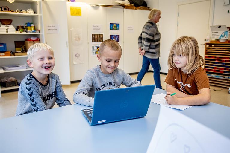 Tre yngre skolelever sidder med computer og har det sjovt