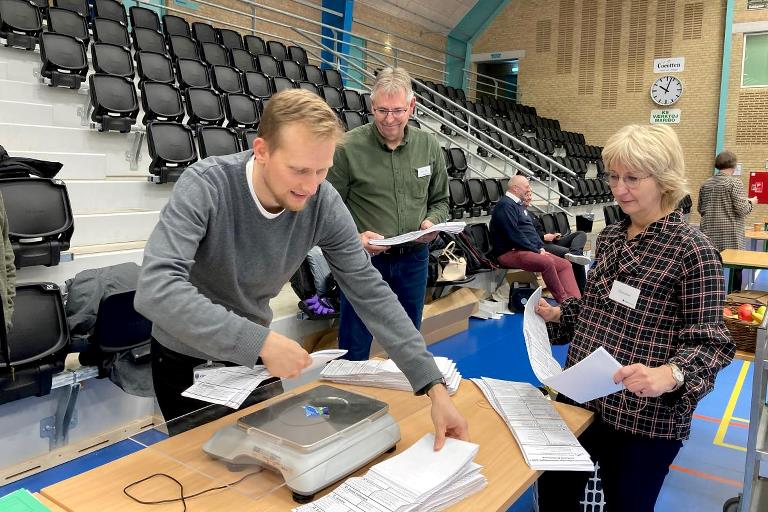 Tre personer kontrollerer stemmersedler på en vægt