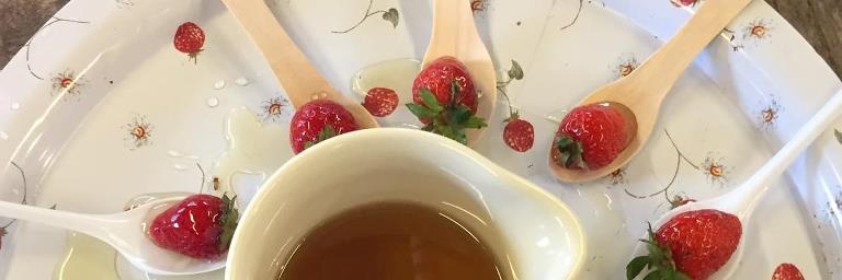Strawberries arranged on spoons on a plate with a jug of syrup